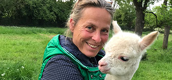 Anne Knein lächelt in die Kamera und hält ein kleines Alpaka auf dem Arm.