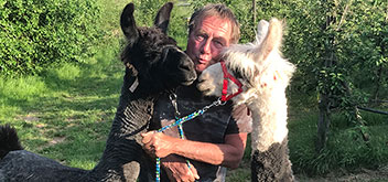 Aloysius Knein steht während einer Lama-Trekking-Tour zwischen zwei sich anschauenden Lamas und schneidet Grimassen.